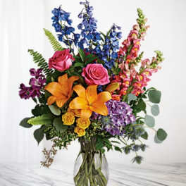 Colorful bouquet with lilies, roses, and tall blue and pink blooms in a glass vase