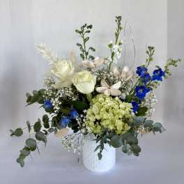 White roses and blue flowers in a white vase with eucalyptus