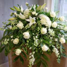White floral arrangement with roses and lilies on a burlap-covered stand