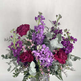 Purple and magenta flowers arranged in a clear glass vase