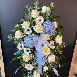 Standing floral spray with white roses, blue hydrangeas, and a ribbon bow