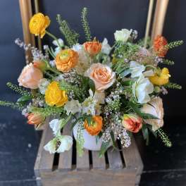 Mixed bouquet of peach, yellow, and white flowers in a white vase