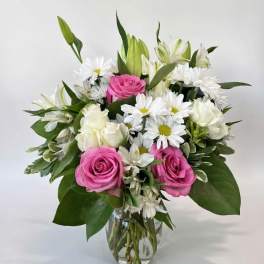 Bouquet of pink roses, white daisies, and white roses in a clear glass vase