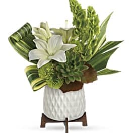 White lily arrangement with green foliage in a white vase