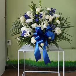 Large white and blue floral spray with a ribbon bow on a stand