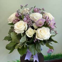 White rose and lavender alstroemeria arrangement in a clear vase with a lavender ribbon