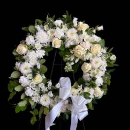 White floral wreath with roses and daisies on a stand, tied with a white ribbon