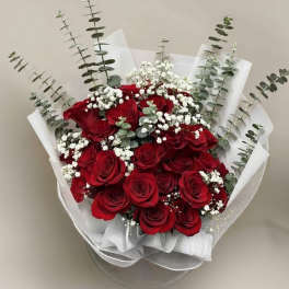 Hand-tied bouquet of red roses with white filler flowers and tall greenery wrapped in white paper.