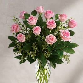 Pink roses arranged in a clear glass vase with greenery