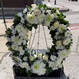 White floral wreath on a stand with roses and daisies