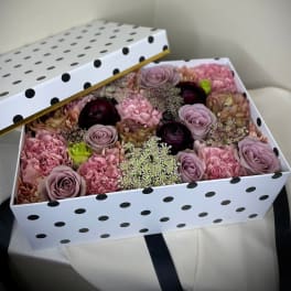 Rectangular polka dot gift box filled with pink and mauve roses and carnations, lid propped open