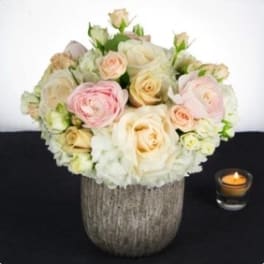 Cream and blush rose bouquet in a textured vase beside a small candle