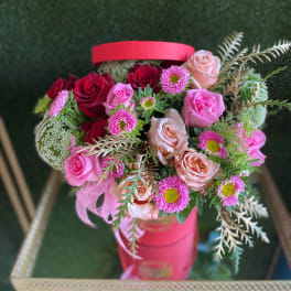 Bouquet of pink and red roses with small pink daisies in a pink hatbox