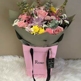 Mixed bouquet of pink roses, yellow blooms, and lavender flowers in a pink gift bag