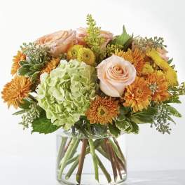 Peach roses and orange mums in a clear glass vase