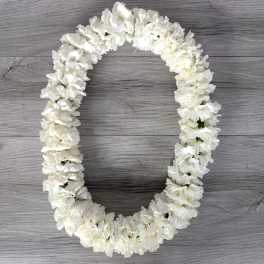 White flower lei arranged in an oval shape on a gray wood surface