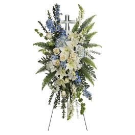 Standing funeral spray of white lilies, roses, and blue flowers on an easel
