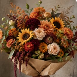 Bouquet of sunflowers, dahlias, and roses wrapped in brown paper