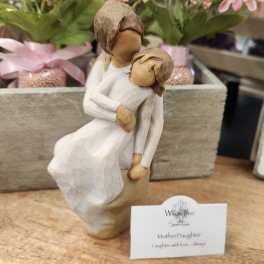 Wooden mother and daughter figurine in front of pink potted flowers