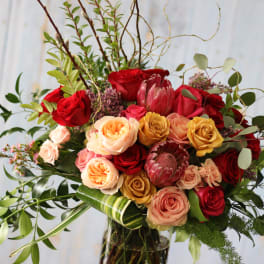 Mixed bouquet of red, peach, and yellow roses with greenery in a glass vase