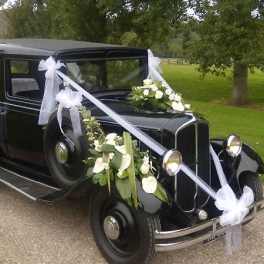 Black vintage car decorated with white ribbons and floral sprays