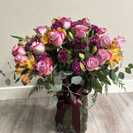 Pink roses and purple flowers in a glass vase with a burgundy ribbon