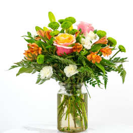 Bright mixed bouquet of roses, orange alstroemeria, green button mums, and white blooms in a clear glass jar.