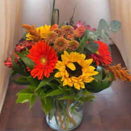 Mixed bouquet of sunflowers, gerbera daisies, and mums in a glass vase