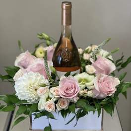 Pink and white roses arranged around a wine bottle in a box
