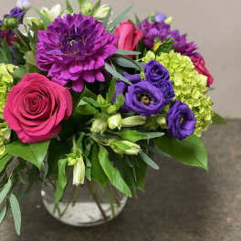 Bouquet of pink roses, purple blooms, and green hydrangeas in a glass vase