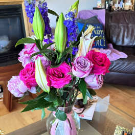 Bouquet of pink roses, purple lilies, and blue delphinium in a glass vase
