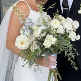 Bride holding a white and pale blue bouquet beside a groom in a black suit