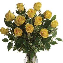 Yellow roses arranged in a clear glass vase with greenery