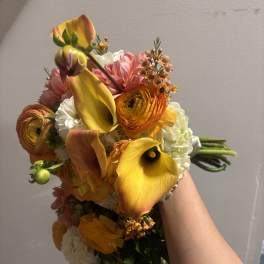 Handheld bouquet with yellow calla lilies, orange ranunculus, and pink blooms