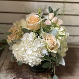 Low round arrangement of peach roses and white hydrangeas in a glass vase