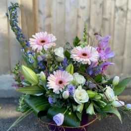 Mixed bouquet with pink gerbera daisies, white roses, and purple flowers in a basket