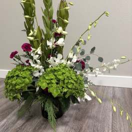 Tall floral arrangement with white orchids, magenta carnations, and green hydrangeas in a black vase