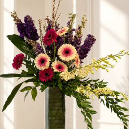 Tall arrangement of purple and pink flowers in a glass vase