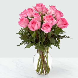 Dozen pink roses arranged in a clear glass vase on a light surface