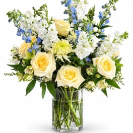 Bouquet of cream roses, white blooms, and blue flowers in a glass vase