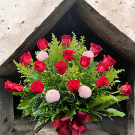 Red roses and pink pompom flowers in a patterned vase with a burgundy ribbon