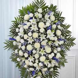 Large white and blue funeral spray with lilies, roses, and palm fronds