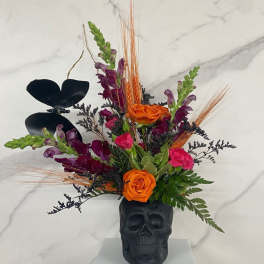 Orange and purple floral arrangement in a black skull vase