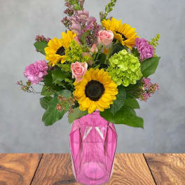 Bouquet of sunflowers, pink roses, and purple flowers in a pink vase