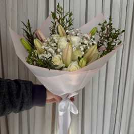 Handheld bouquet of white roses and lily buds wrapped in pale pink paper