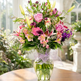 Mixed bouquet of pink and purple flowers in a glass vase with a lavender ribbon