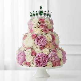Tiered pink and white floral cake with a jeweled green crown topper