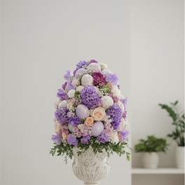 Purple and pink floral arrangement with decorative eggs in a white urn
