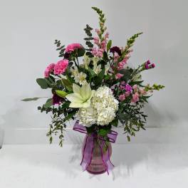 Mixed pink and white flowers in a glass vase with a purple ribbon