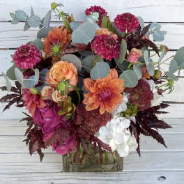 Mixed bouquet of orange, pink, and white flowers in a glass vase